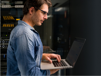 White male IT professional working on laptop in data center server room